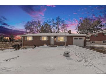 Brick ranch house with attached garage, snow-covered yard, and twilight sky at 12008 W Mexico Pl, Lakewood, CO 80228