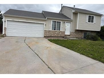Tan two-story home featuring an attached garage and stone accents, perfect for suburban living at 1415 S Pitkin Ct, Aurora, CO 80017