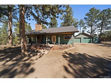 Charming single-story home with a stone chimney and a detached two-car garage nestled among mature trees at 28539 Douglas Park Rd, Evergreen, CO 80439