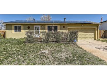 Ranch style home with solar panels, two-car garage, and front yard with mature bushes at 15645 E Floyd Ave, Aurora, CO 80013
