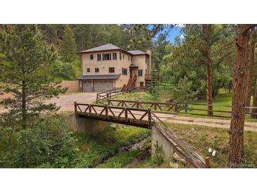 Charming two-story home with a bridge leading to the property and a three car garage at 27756 Troublesome Gulch Rd, Evergreen, CO 80439
