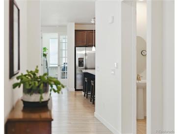 Hallway view showcasing wood floors, leading to the kitchen and a room with glass doors at 8844 S Sicily Ct, Aurora, CO 80016