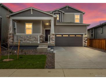 Charming two-story home with a covered porch, stone accents, and a two-car garage at sunset at 571 Homestead Ave, Brighton, CO 80601