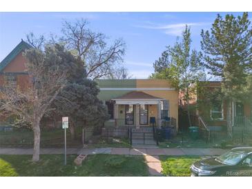 Charming exterior view of yellow and green house with dark iron gate and landscaping at 2614 Curtis St, Denver, CO 80205