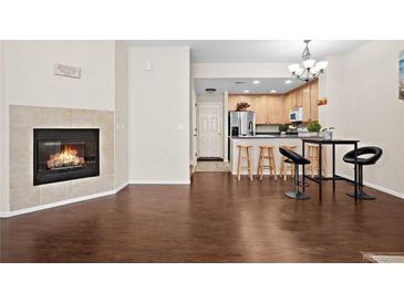 Open-concept living room with hardwood floors, fireplace, and kitchen with bar seating at 15945 E Geddes Dr # 54, Aurora, CO 80016
