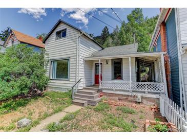 Charming home with a red front door and a cozy porch, nestled amidst lush greenery and a bright sky backdrop at 1324 Virginia St, Idaho Springs, CO 80452
