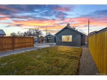 The fenced backyard features a manicured lawn and a detached garage under a colorful sunset sky at 469 S Perry St, Denver, CO 80219