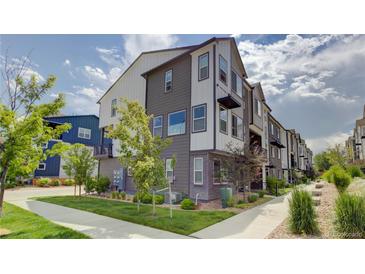 A modern townhouse with gray and white siding, lush green lawn, and young trees at 12225 W 57Th Pl, Arvada, CO 80002