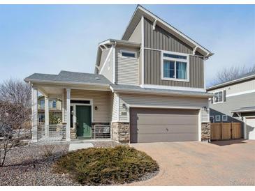 Two-story home featuring stone accents, a covered porch, a two-car garage, and a well-maintained landscape at 18066 E 104Th Way, Commerce City, CO 80022