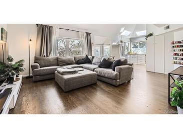 Bright living room features hardwood floors, large window, and comfortable gray sectional couch and ottoman at 1300 S Monaco Pkwy # 12, Denver, CO 80224