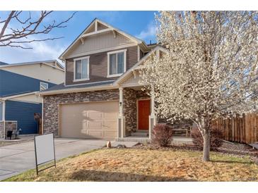 Charming two-story home with a stone and siding facade, manicured lawn, and a blooming tree in the front yard at 13563 E 106Th Pl, Commerce City, CO 80022