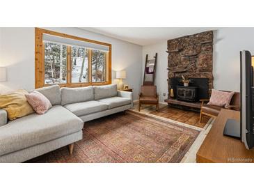 Cozy living room featuring a stone fireplace, comfortable sofa and a view of the trees at 28254 Tresine Dr, Evergreen, CO 80439