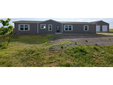 Gray home exterior featuring white trim, a gravel yard, with grass and a separate garage in the background at 11595 Pass Me By Rd, Strasburg, CO 80136