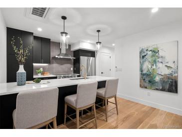 Modern kitchen featuring black cabinets, stainless steel appliances, and a bright white countertop island with chairs at 2451 Lawrence St # 2, Denver, CO 80205