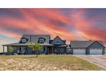 Gray two-story house with a large front porch, three-car garage, and beautiful sunset at 402 S County Road 129, Bennett, CO 80102