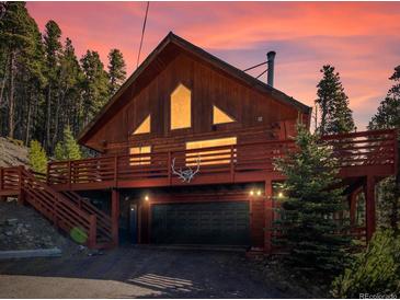 Charming two-story cabin featuring a spacious deck, garage, and picturesque wooded surroundings at sunset at 451 Harris Dr, Idaho Springs, CO 80452