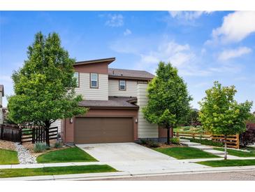 Charming two-story home with a brown and beige exterior, a well-manicured lawn, mature trees, and a two car garage at 17258 E 109Th Ave, Commerce City, CO 80022
