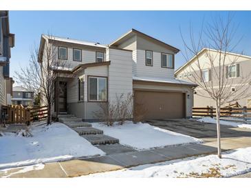 Two-story home with a two-car garage and a manicured lawn and a snow covered front yard at 18012 E 107Th Ave, Commerce City, CO 80022