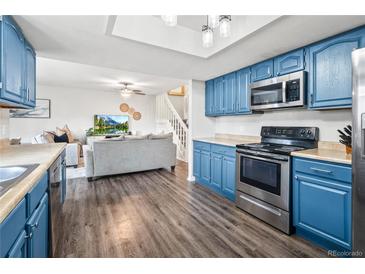 Open kitchen with stainless steel appliances, blue cabinets, and hardwood floors adjoins a living room with staircase at 1080 S Yampa St, Aurora, CO 80017