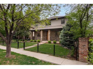 Charming two-story home with a well-manicured front yard, a black metal fence, and mature trees at 1927 S Grant St, Denver, CO 80210