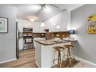 Updated kitchen with white cabinets, breakfast bar and stools, stainless steel appliances, and modern lighting at 710 S Clinton St # 3A, Denver, CO 80247