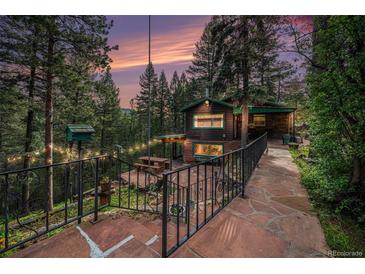 Charming cabin exterior with stone walkway, inviting patio, and lush green surroundings at twilight at 5672 Santa Clara Rd, Indian Hills, CO 80454