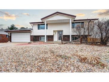 Split-level home featuring a white facade, brick accents, a two-car garage, and low-maintenance landscaping at 301 S Troy St, Aurora, CO 80012
