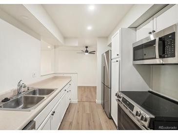 Modern kitchen features stainless steel appliances, white cabinets and light countertops; open to dining area with wood floors at 1113 W 112Th Ave # B, Denver, CO 80234