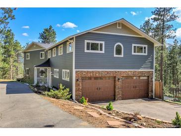 Two-story home with a stone-clad garage and gray siding, surrounded by trees and a blue sky at 4574 Picutis Rd, Indian Hills, CO 80454