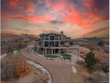 Stunning home with a driveway, backyard patio, and water feature at sunset at 3520 Castle Butte Dr, Castle Rock, CO 80109