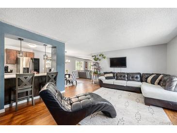 Open-concept living room with hardwood floors, leather sectional, and view of kitchen at 4844 E 110Th Pl, Thornton, CO 80233
