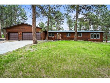 Charming wood home with a lush green lawn and a two-car attached garage surrounded by mature trees at 26499 West St, Conifer, CO 80433
