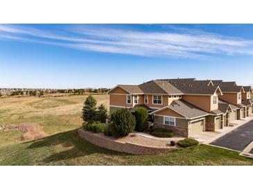 Inviting townhome exterior with neutral siding, mature landscaping, and a retaining wall, set against an expansive field at 3661 S Perth Cir # 6-101, Aurora, CO 80013