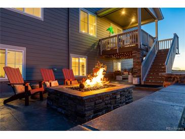 Relaxing backyard patio with stone fire pit, lounge chairs, and second story deck under warm lighting at 17851 Herrera Dr, Parker, CO 80134