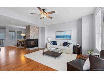 Bright living room with hardwood floors, stone fireplace, ceiling fan, and view into dining area at 10204 Ridgegate Cir, Lone Tree, CO 80124