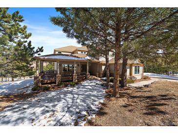 Tan two story house with a covered patio and large trees in the front yard with snow on the ground at 1366 Killington Ct, Evergreen, CO 80439