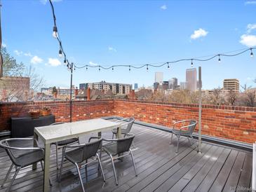 Charming rooftop patio with city views, string lights, table and chairs on a wood surface and brick wall at 1130 N N Pennsylvania St # 306, Denver, CO 80203
