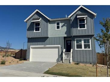 Beautiful two-story home featuring gray siding, white garage door, and charming front entrance under a clear blue sky at 16947 W 92Nd Dr, Arvada, CO 80007