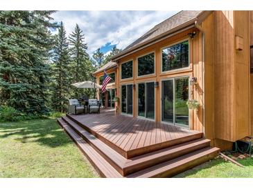 Beautiful home featuring a large wooden deck with ample seating overlooking a well-manicured lawn at 25257 Snyder Ave, Conifer, CO 80433