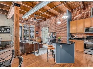 Open-concept living room with exposed brick, wooden beams, and modern kitchen island at 2960 Inca St # 317, Denver, CO 80202