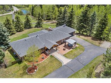 An aerial view of a ranch-style home with a brick patio, pergola, and lush landscaping surrounded by mature trees at 27436 Kennedy Gulch Rd, Conifer, CO 80433
