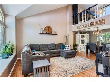 Spacious living room with high ceilings, a cozy gray sectional, and an open view to the dining area at 9492 Crestmore Way, Highlands Ranch, CO 80126