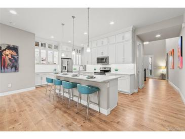 Bright kitchen featuring white cabinets, a large island with bar seating, and pendant lighting over light wood-look floors at 17720 W 94Th Dr, Arvada, CO 80007