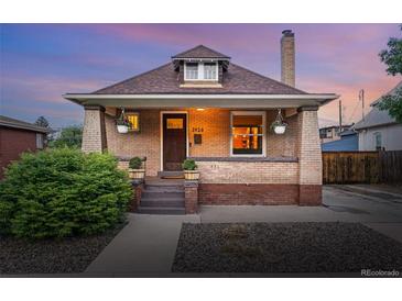 Charming brick home featuring a cozy front porch, well-manicured landscaping, and warm exterior lighting at 3928 Zuni St, Denver, CO 80211