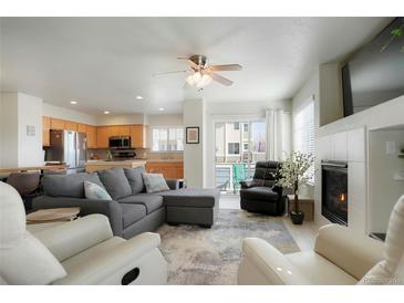 Open-concept living room boasts a gray sofa, ceiling fan, fireplace and seamless access to the kitchen and outdoor area at 15800 E 121St Ave # 4G, Brighton, CO 80603