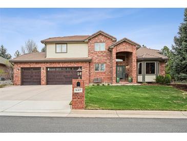 Charming brick home featuring a three-car garage, manicured lawn, and covered entryway at 14417 W 57Th Pl, Arvada, CO 80002