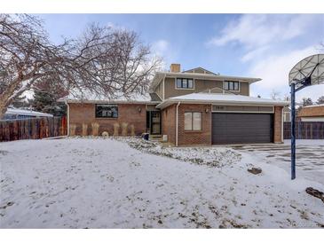 Two-story home with a brick and brown siding, attached garage, and snow-covered front yard at 7835 Nelson St, Arvada, CO 80005