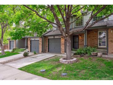 Charming townhome featuring brick accents, a gray garage door, and a well-manicured lawn with a mature shade tree at 1953 E 102Nd Cir, Thornton, CO 80229