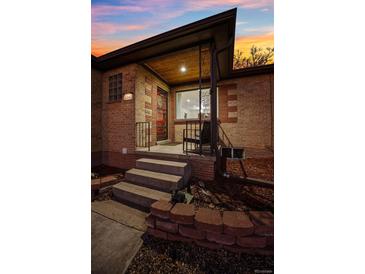 Charming brick home showcasing a cozy covered front porch with wrought iron details at twilight at 2042 Jamaica St, Aurora, CO 80010