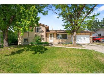 A well-kept lawn complements this charming two-story home with mature trees and a welcoming front entrance at 6953 Ingalls St, Arvada, CO 80003